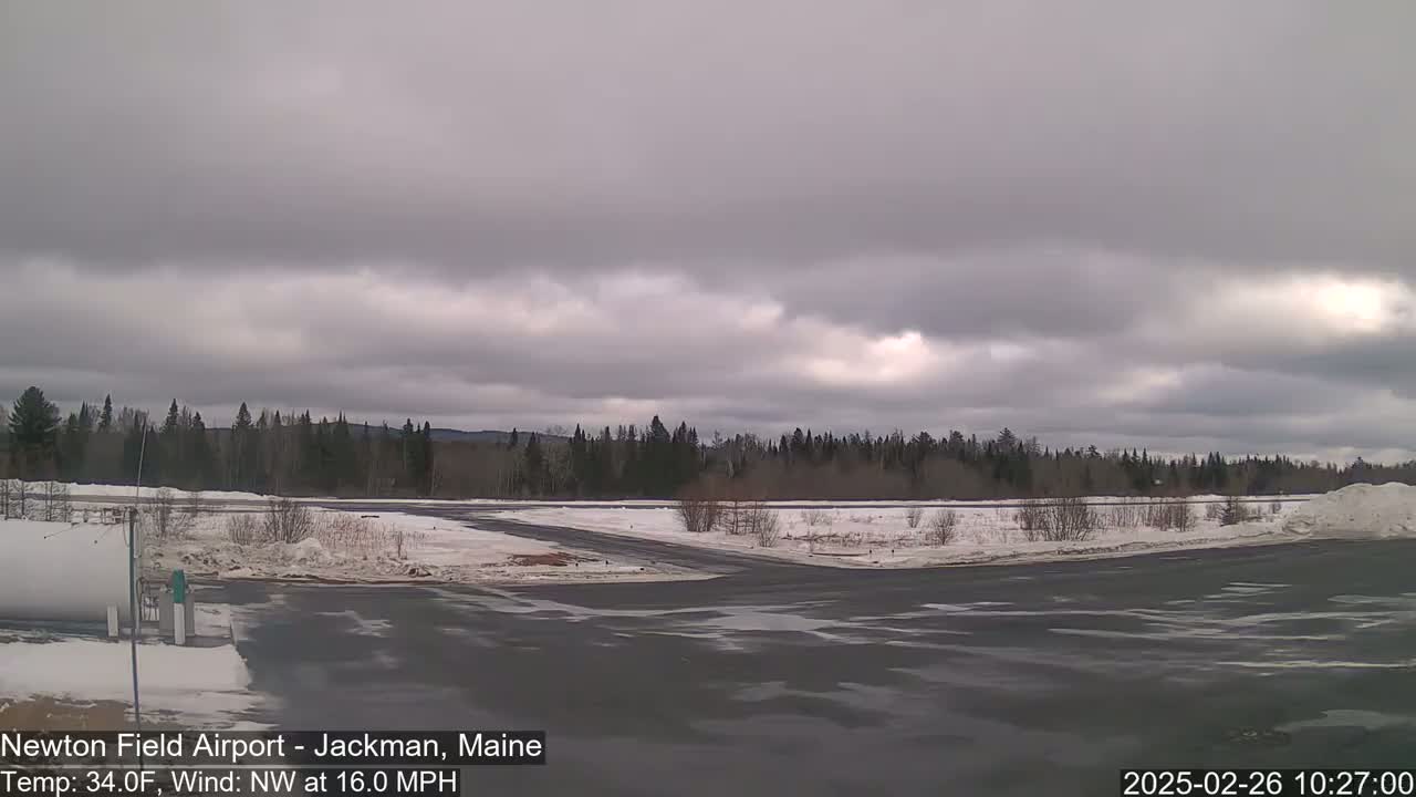 A snow-covered airfield with a dark gray, overcast sky and a 16 mph northwest wind.