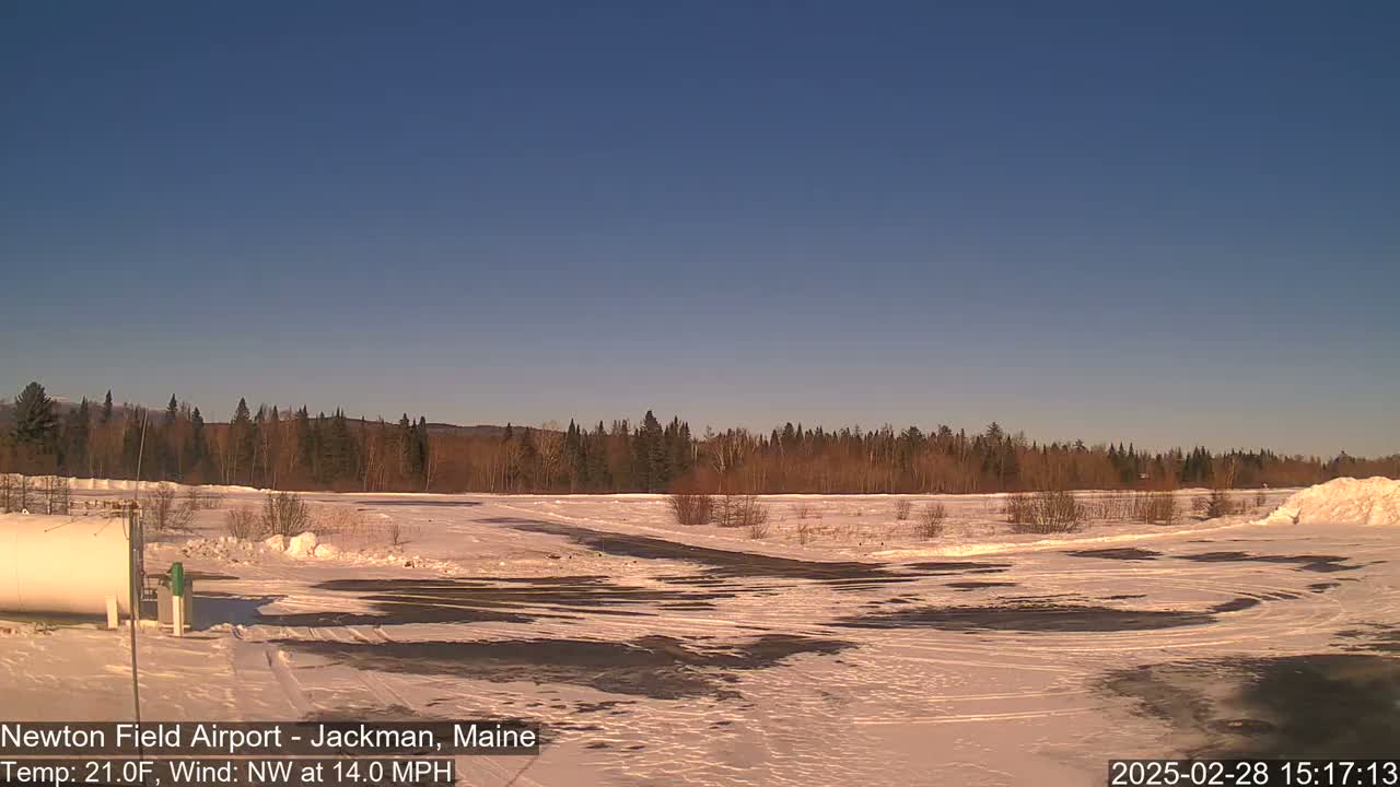 A snow-covered airfield, under a clear blue sky, is bordered by a line of bare winter trees.