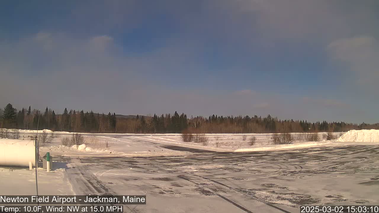 A snow-covered airfield with a line of trees in the background under a mostly clear, bright sky.