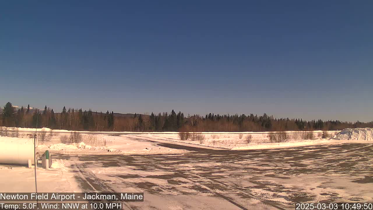A snow-covered airfield with a background of trees and distant mountains under a clear blue sky.