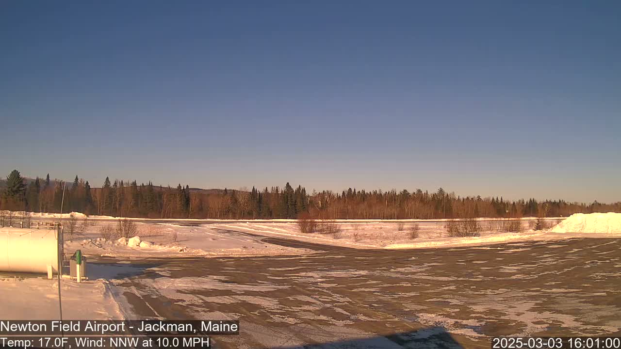 A mostly clear, cold, and windy day reveals a snow-covered airfield bordered by a line of trees.