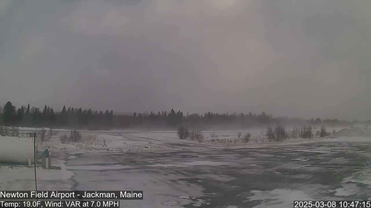 A snow-covered airfield is visible under an overcast sky with a light wind blowing.