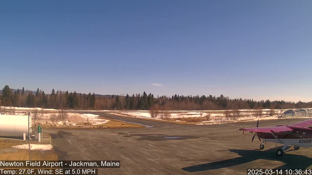 A small airplane sits on a tarmac next to a snow-dusted airfield under a clear blue sky.