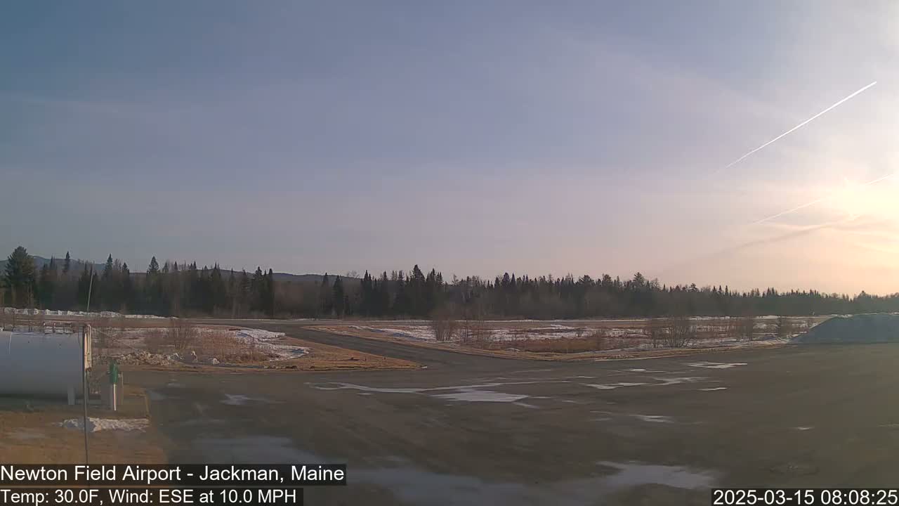 A mostly clear, cold morning at an airfield with a tree line in the background and patches of snow and ice on the ground.