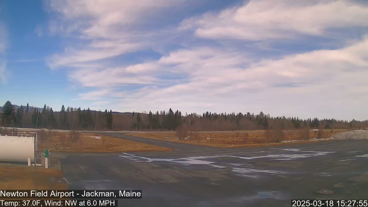 A mostly sunny day at a small airport with a mostly barren landscape and a line of trees in the background.