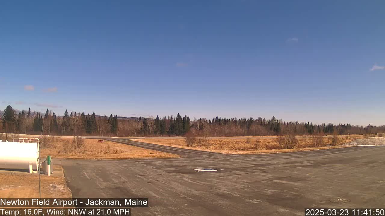 A small airport tarmac with a background of trees and a mostly clear blue sky, under windy, 16°F weather conditions.
