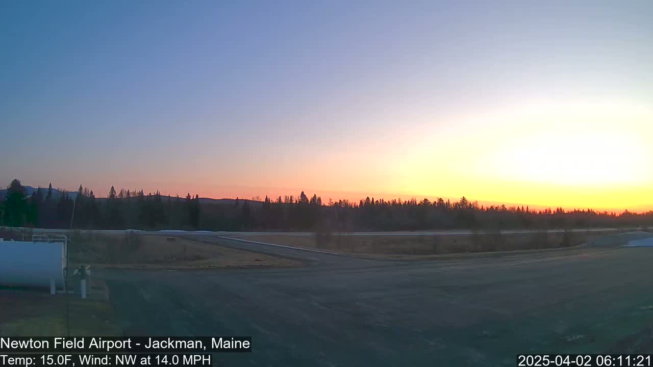 A sunrise illuminates a flat, paved area near a treeline, with a northwest wind at 14 mph and a temperature of 15°F.