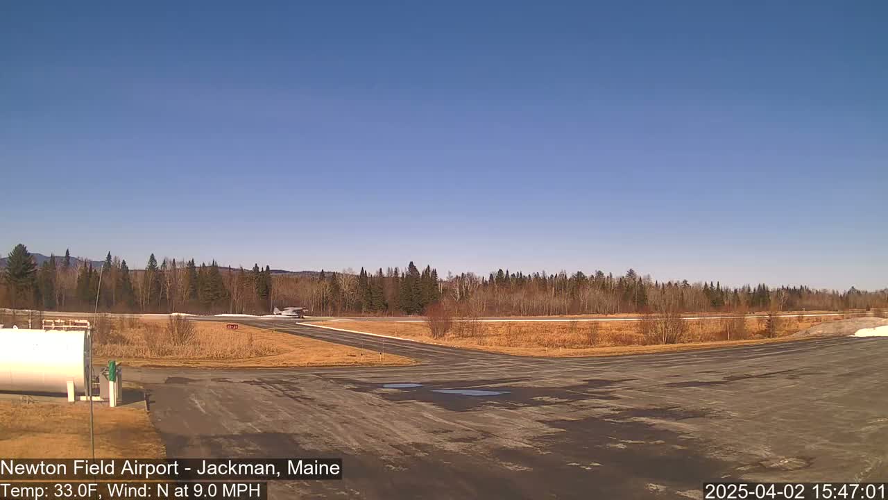 A small airplane is on a runway at a small airport surrounded by trees under a clear blue sky.