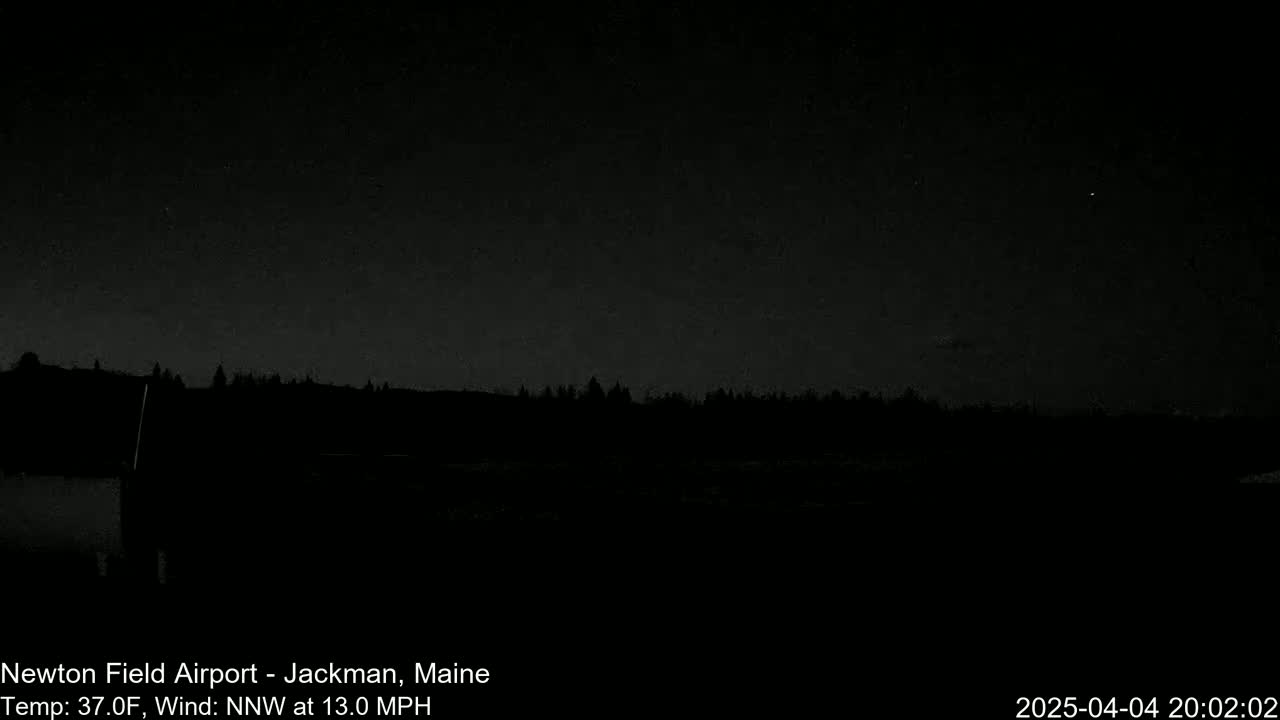 A nighttime, low-light view of a dark landscape featuring a silhouetted tree line under a mostly clear, dark sky with a 37°F temperature and a 13 mph north-northwest wind.