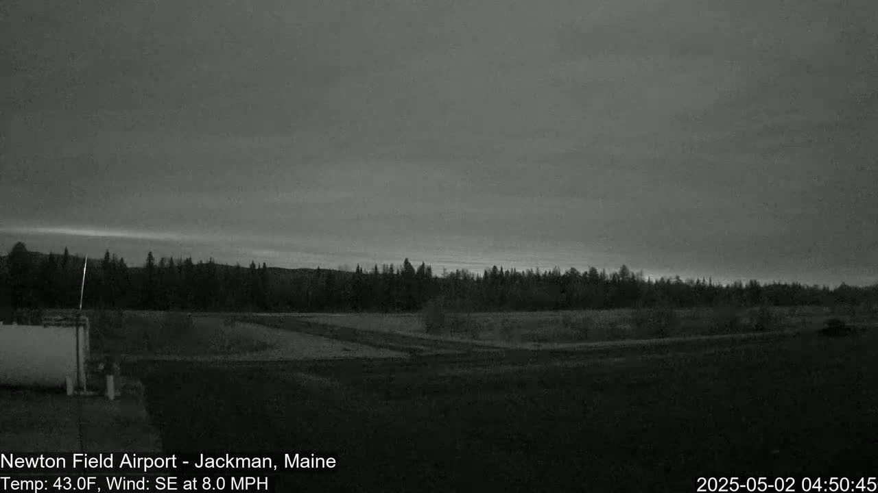 A dark, overcast sky hangs over a flat landscape of trees and fields under a southeast wind.