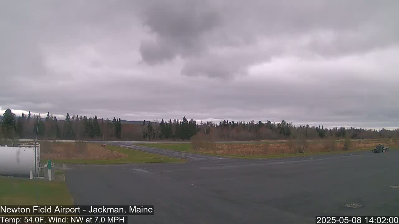A mostly cloudy, overcast day at an airfield shows a runway and surrounding wooded area.