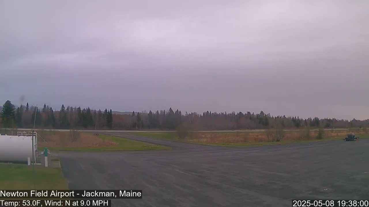 A mostly cloudy airfield with a dark asphalt runway and a line of trees in the background.