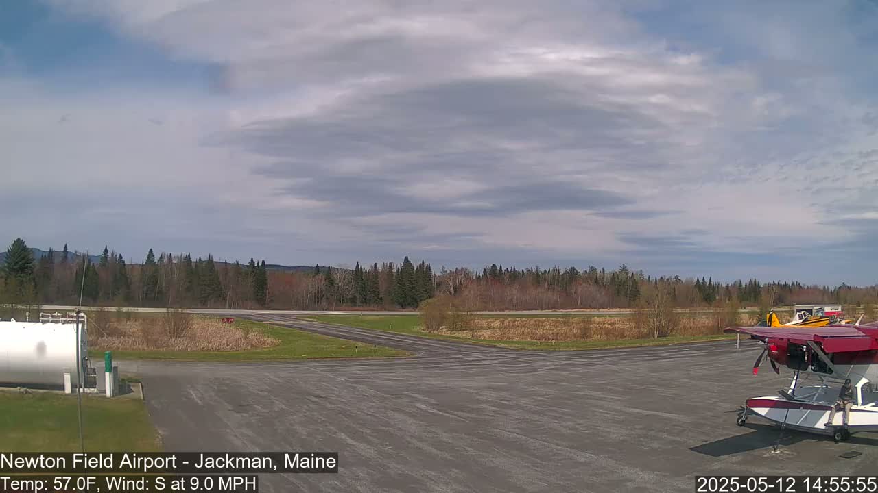 A small airport with a seaplane and other aircraft is visible under a partly cloudy sky with a south wind.