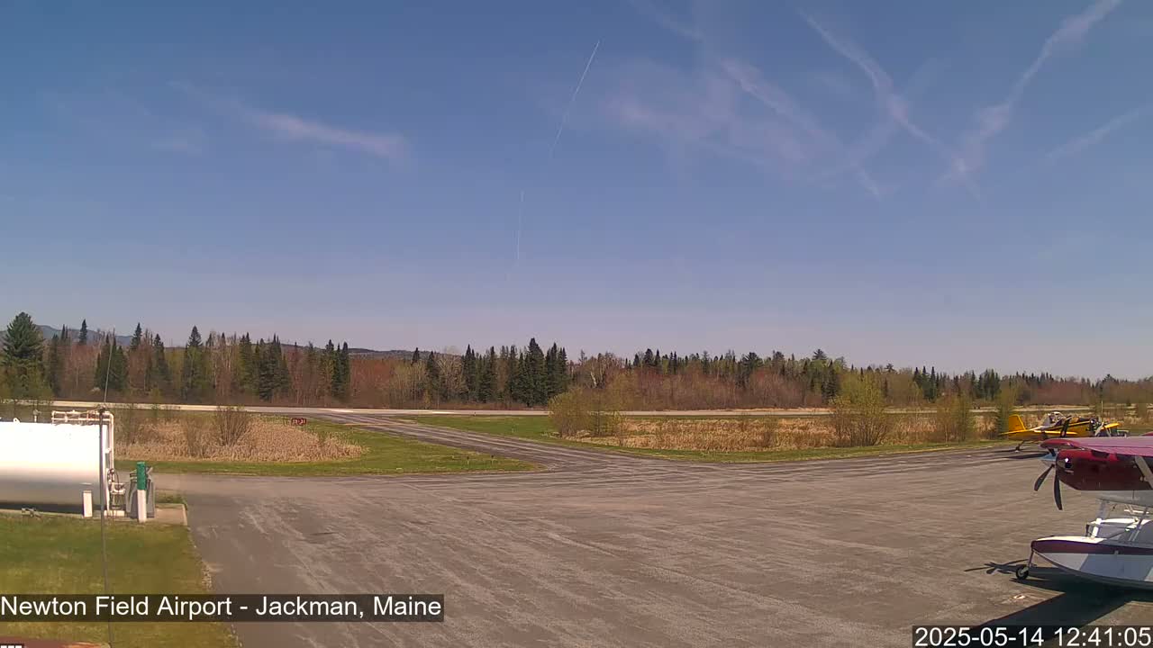 A small airport tarmac with several small airplanes parked, under a clear blue sky with a few contrails.