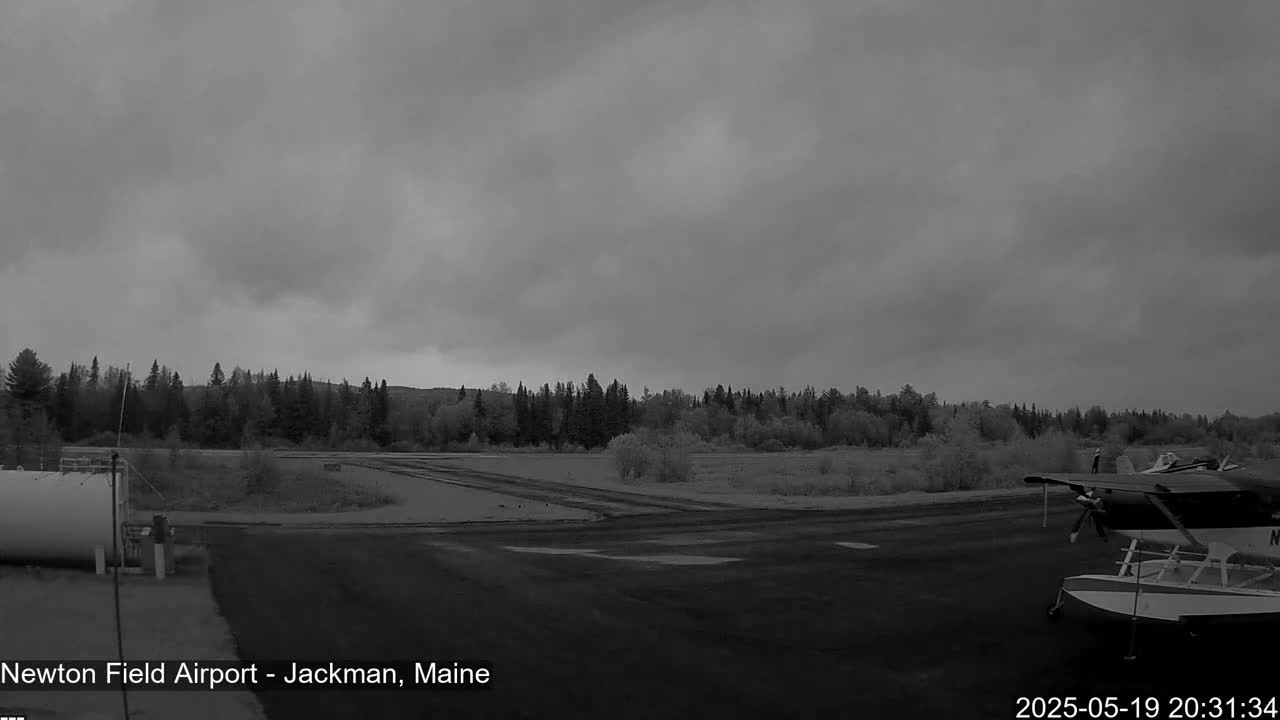A small airplane sits on a tarmac at an airport next to a fuel tank, under an overcast sky.