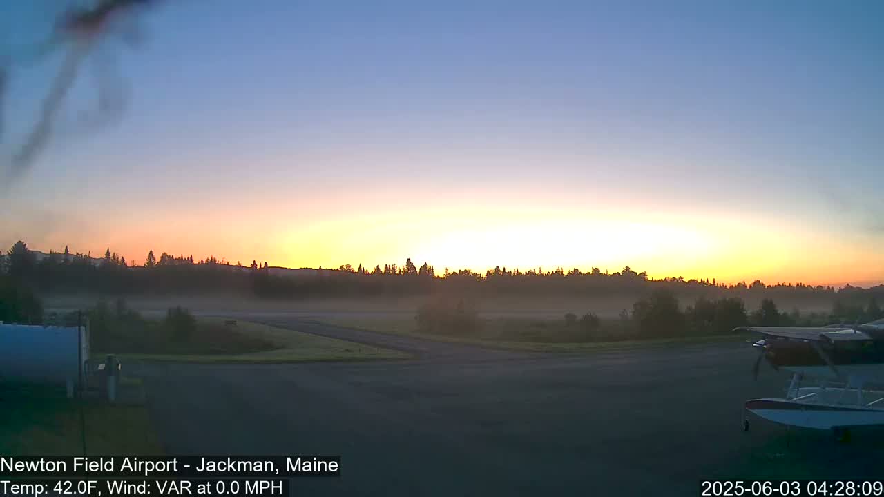 A hazy sunrise over a flat, grassy airfield with a seaplane parked on the tarmac.