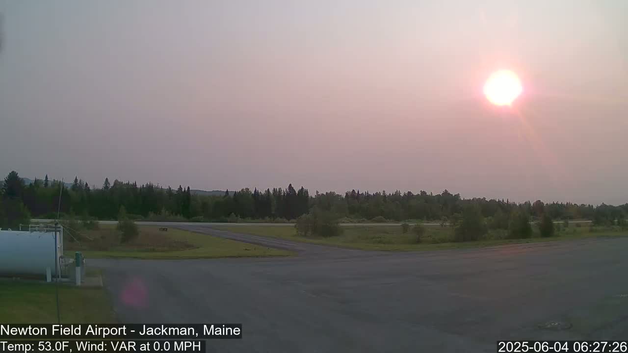 A hazy sunset illuminates an airport runway and surrounding wooded area.