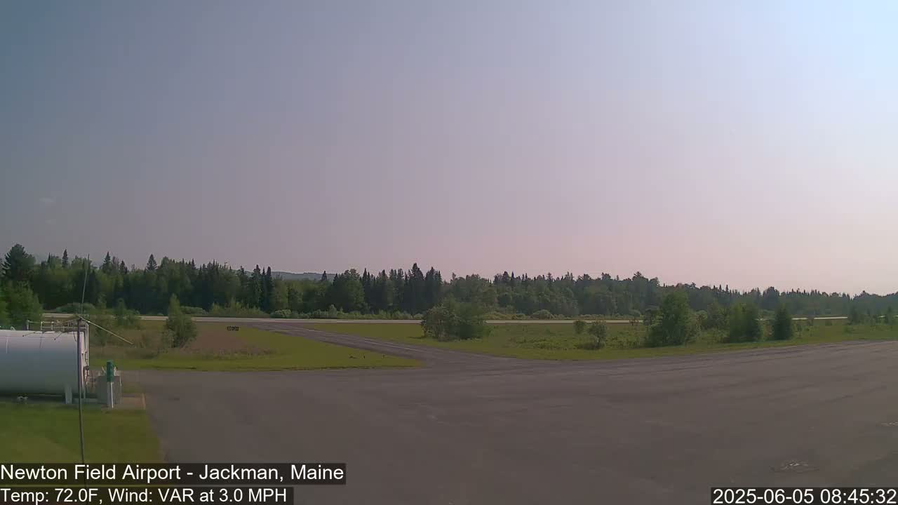 A clear, sunny day reveals an airfield with a paved runway and grassy areas, bordered by a line of trees.