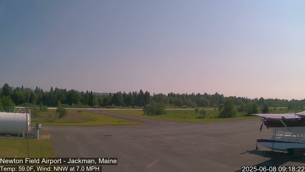 A small airplane sits on a tarmac at an airport surrounded by a green forest under a clear sky.