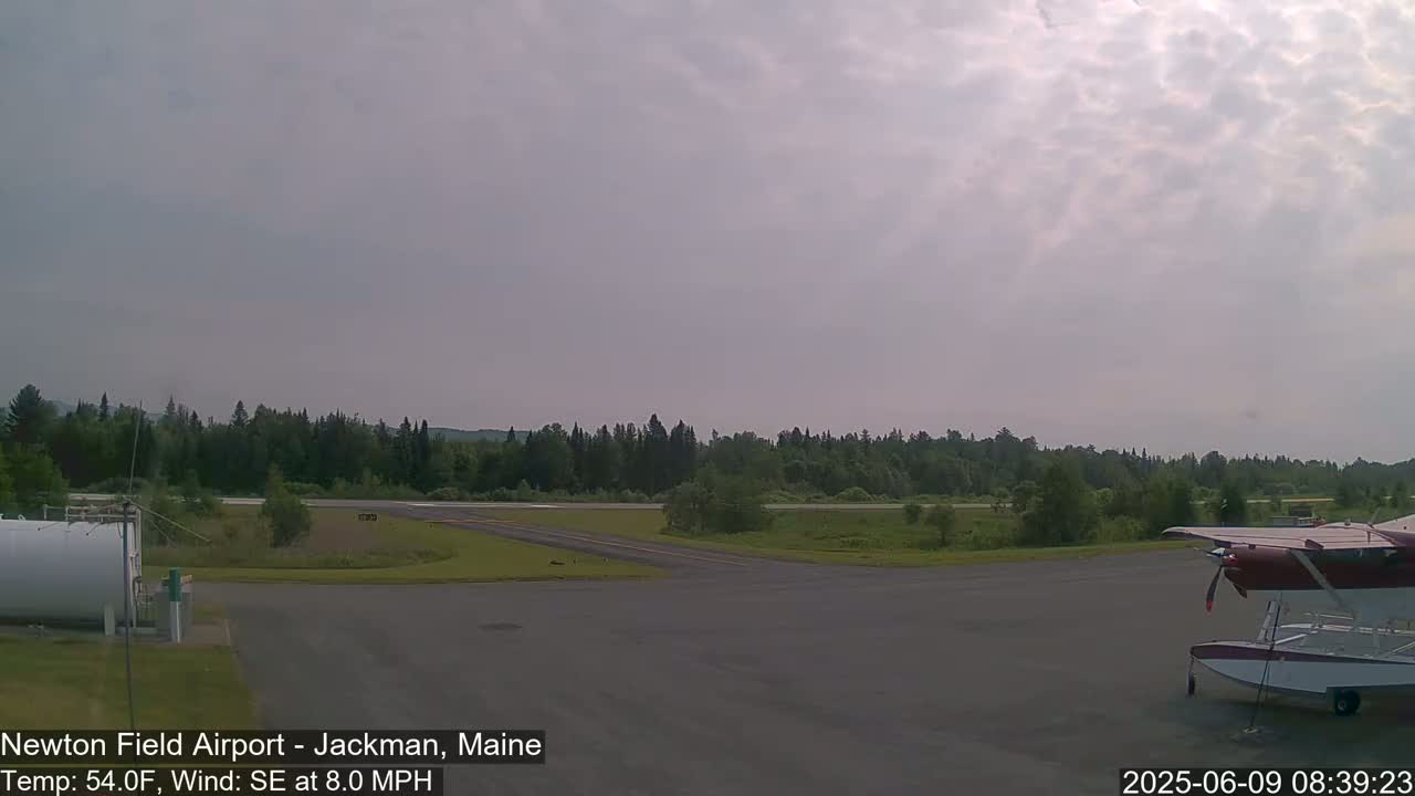A small airport with a seaplane parked on the tarmac, under a mostly cloudy sky.