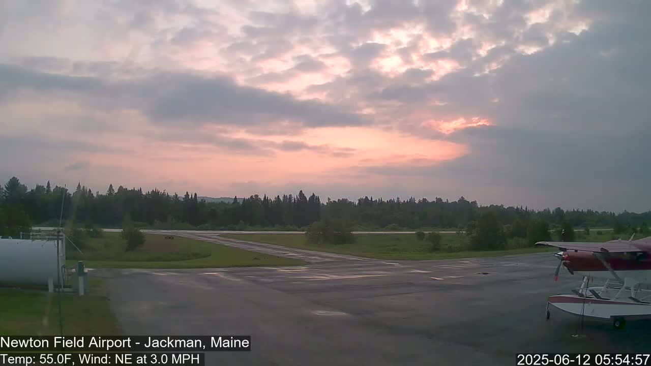 A small airplane sits on an airport tarmac at dawn under a mostly cloudy, pinkish sky.