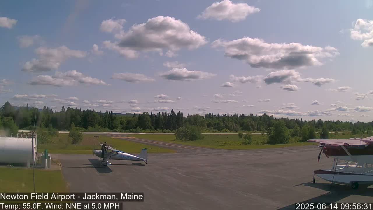 A small airplane is parked on an airfield under a partly cloudy sky.