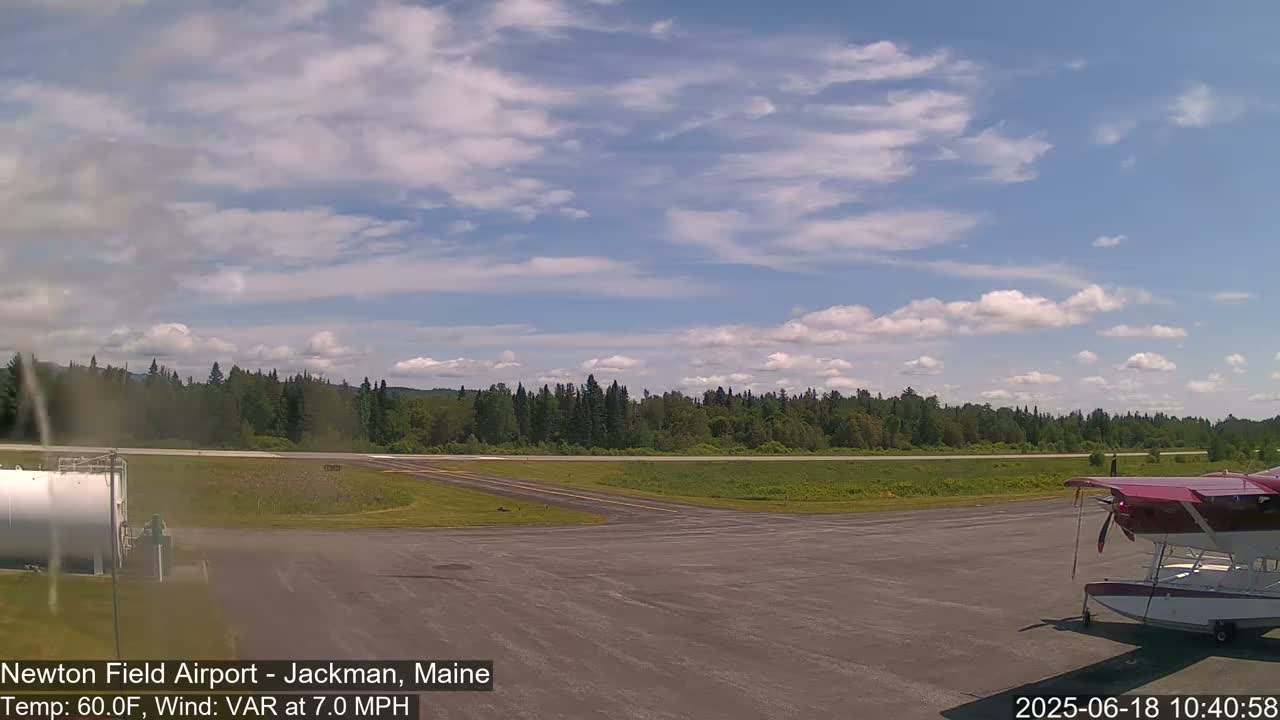 A seaplane sits on a tarmac at an airport with a line of trees and a partly cloudy sky.
