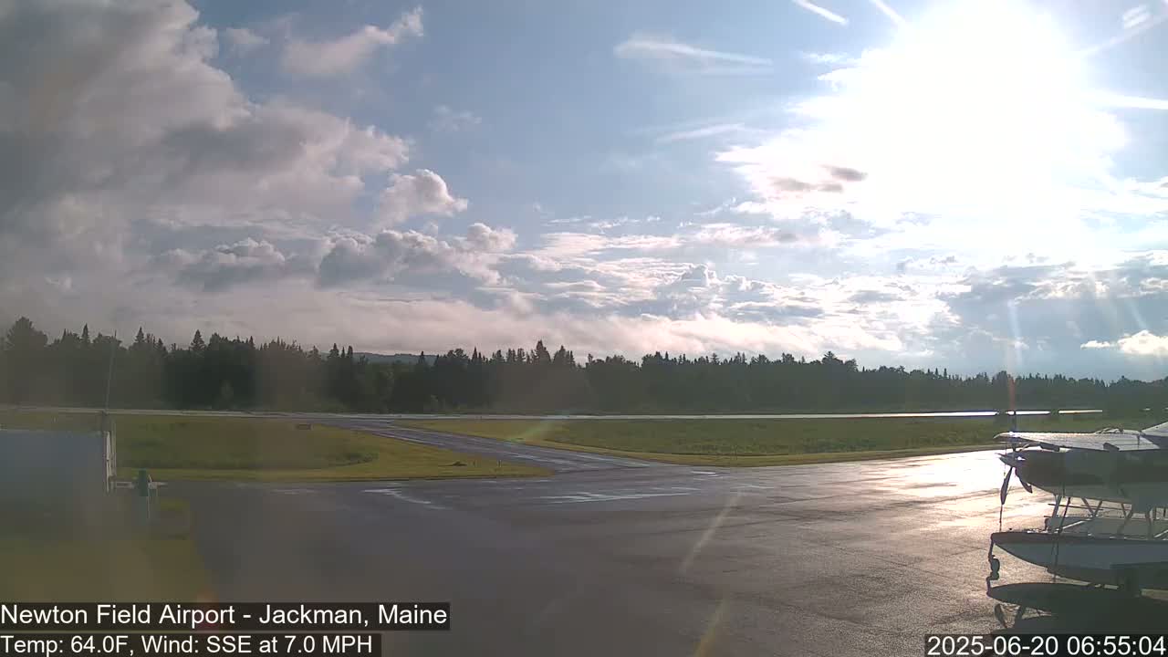 A partly cloudy sky illuminates a small airport with a seaplane parked on the tarmac.