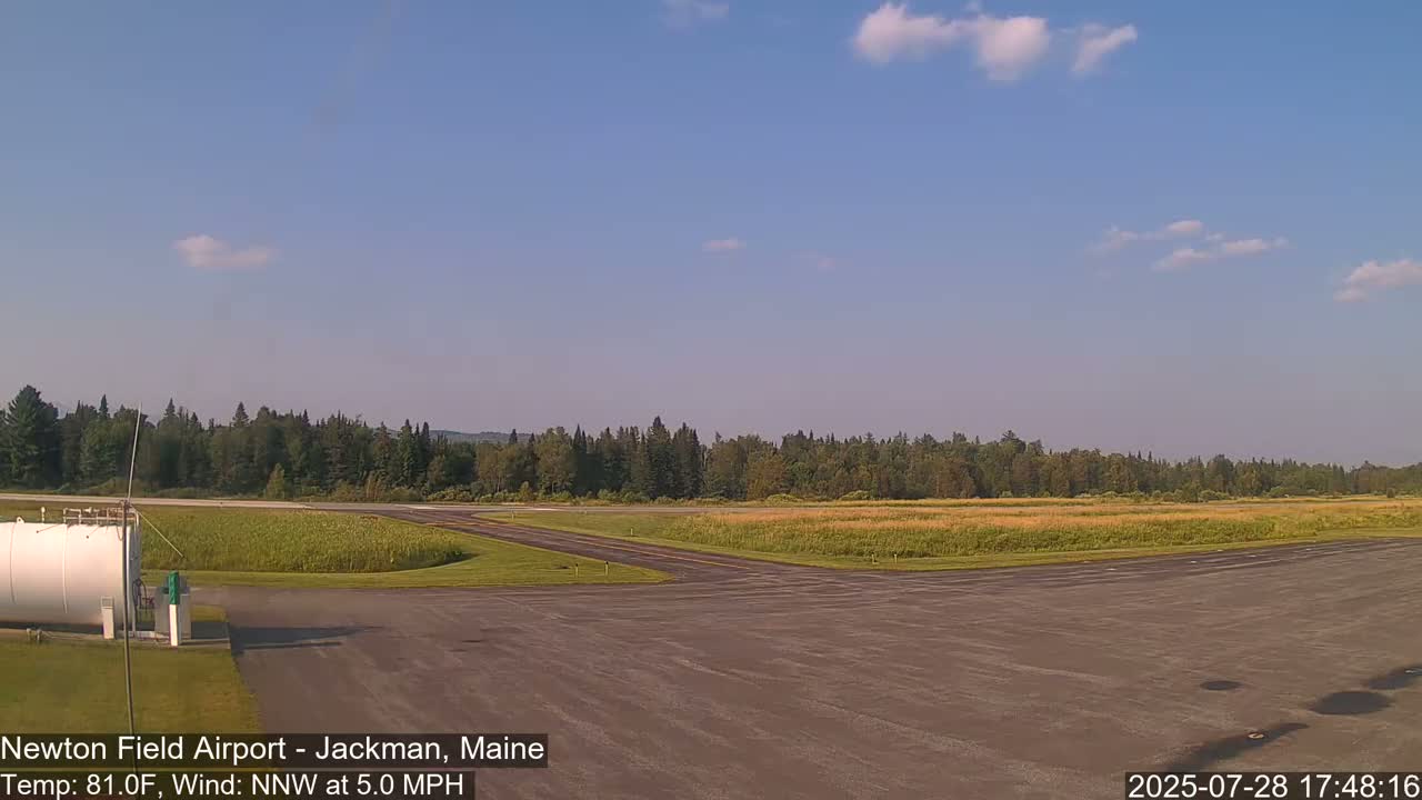A mostly sunny airfield with a grassy field and trees in the background, under a light NNW wind.