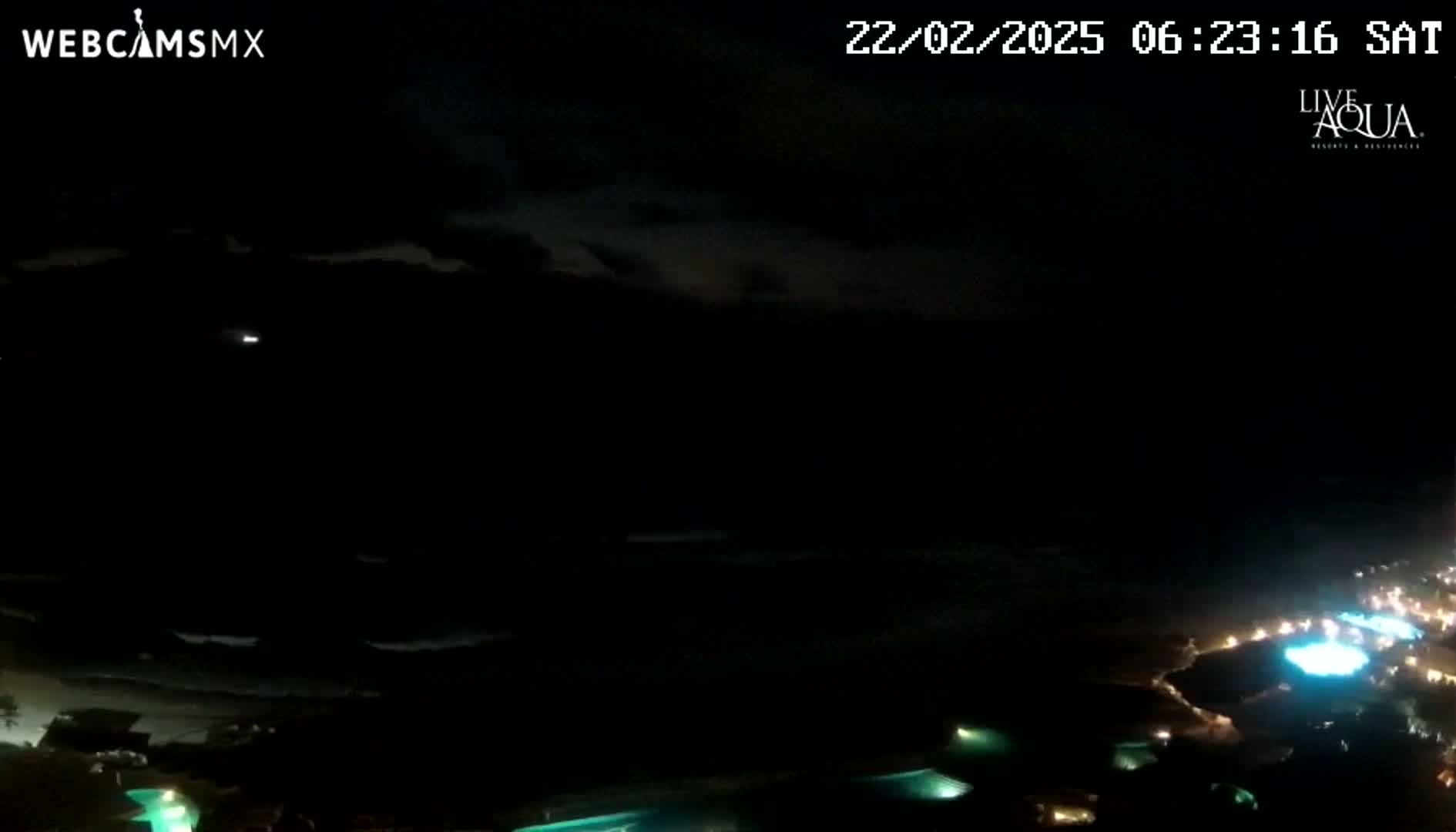 A nighttime, overcast view of a coastline with illuminated pools and a dark ocean.