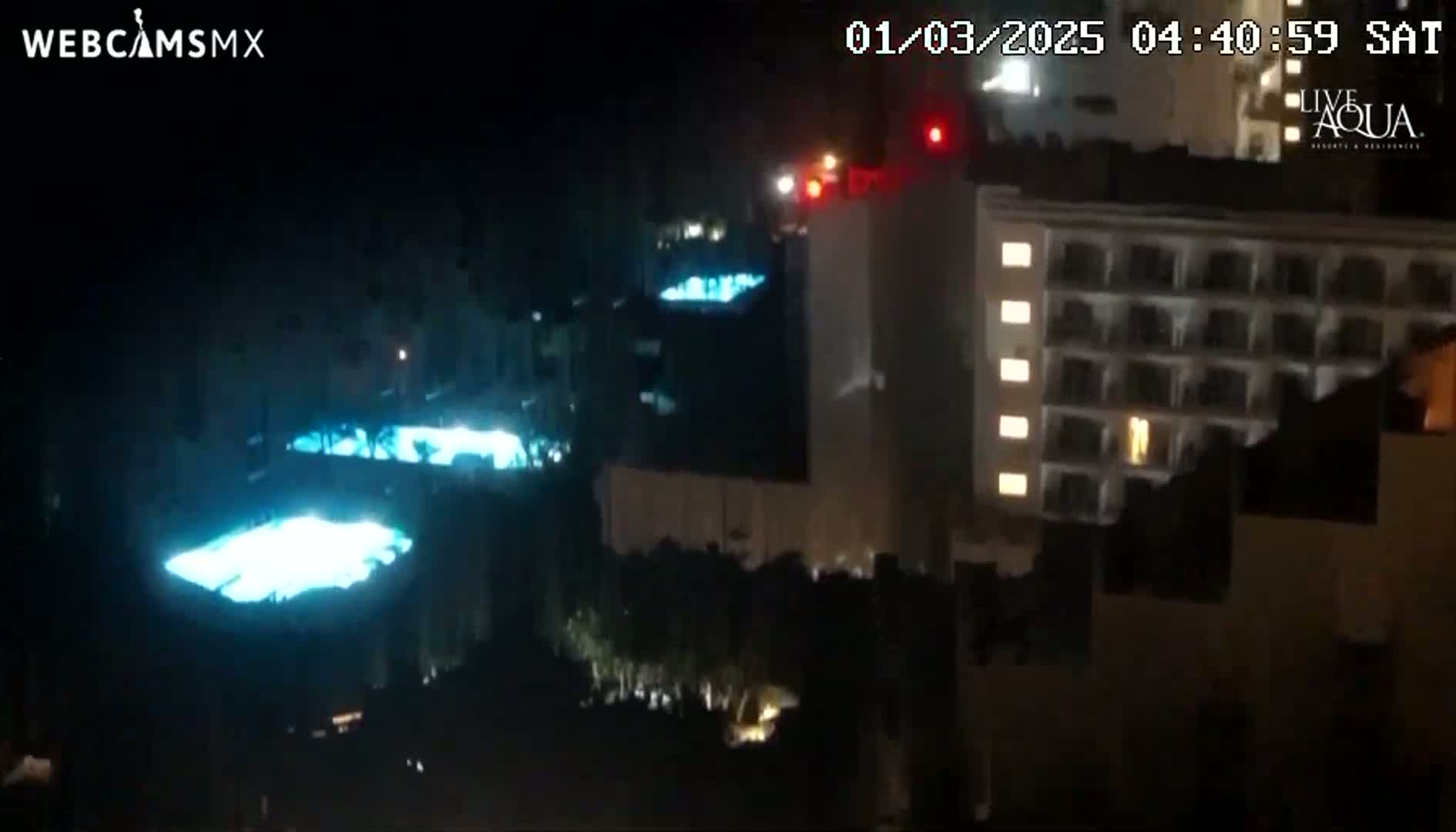 At night, illuminated swimming pools are visible near a multi-story building.