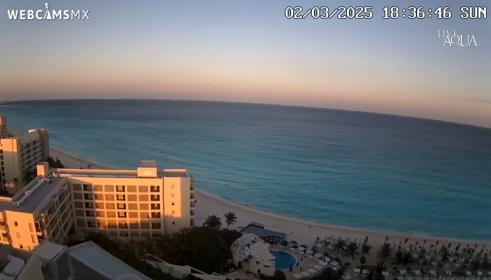 A high-angle view shows a beach with turquoise water at sunset, featuring several hotel buildings and palm trees.