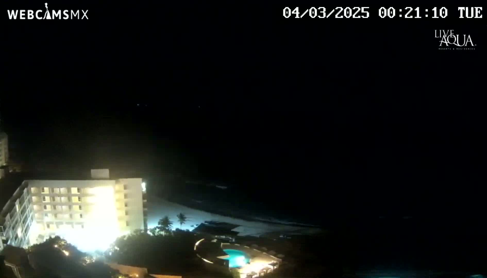 A brightly lit, multi-story building is seen at night next to a dark ocean under a clear, starlit sky.