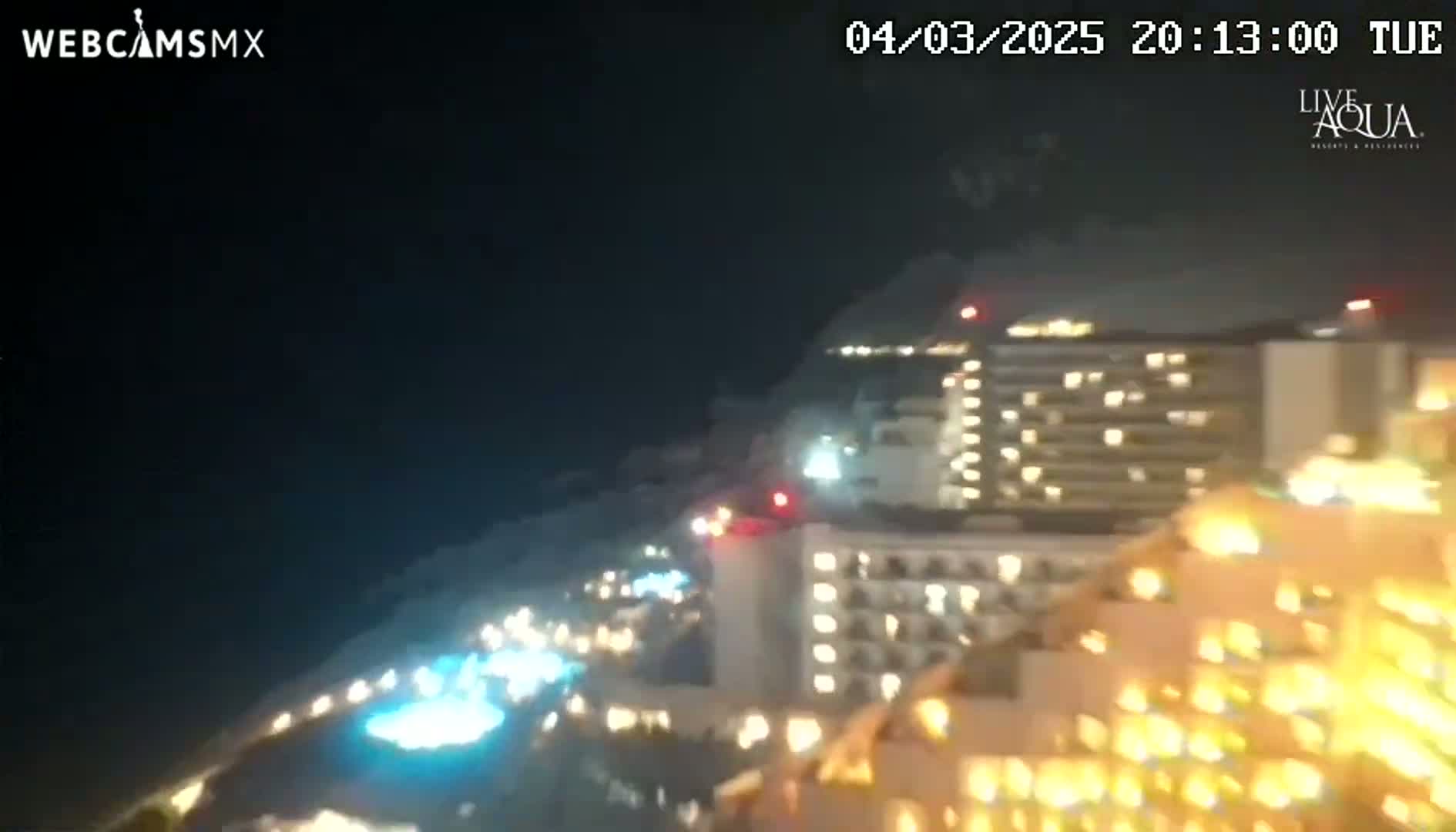 A nighttime, long shot of brightly lit buildings along a coastline under a dark sky.
