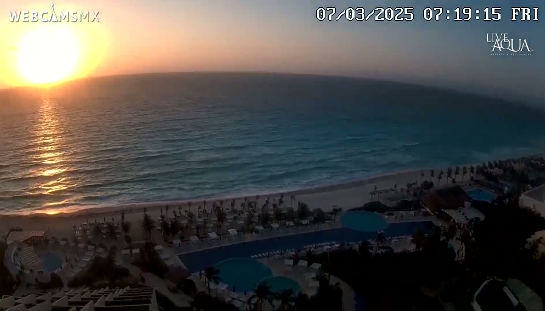 A sunrise over a beach with a resort featuring multiple pools is visible from an elevated vantage point.