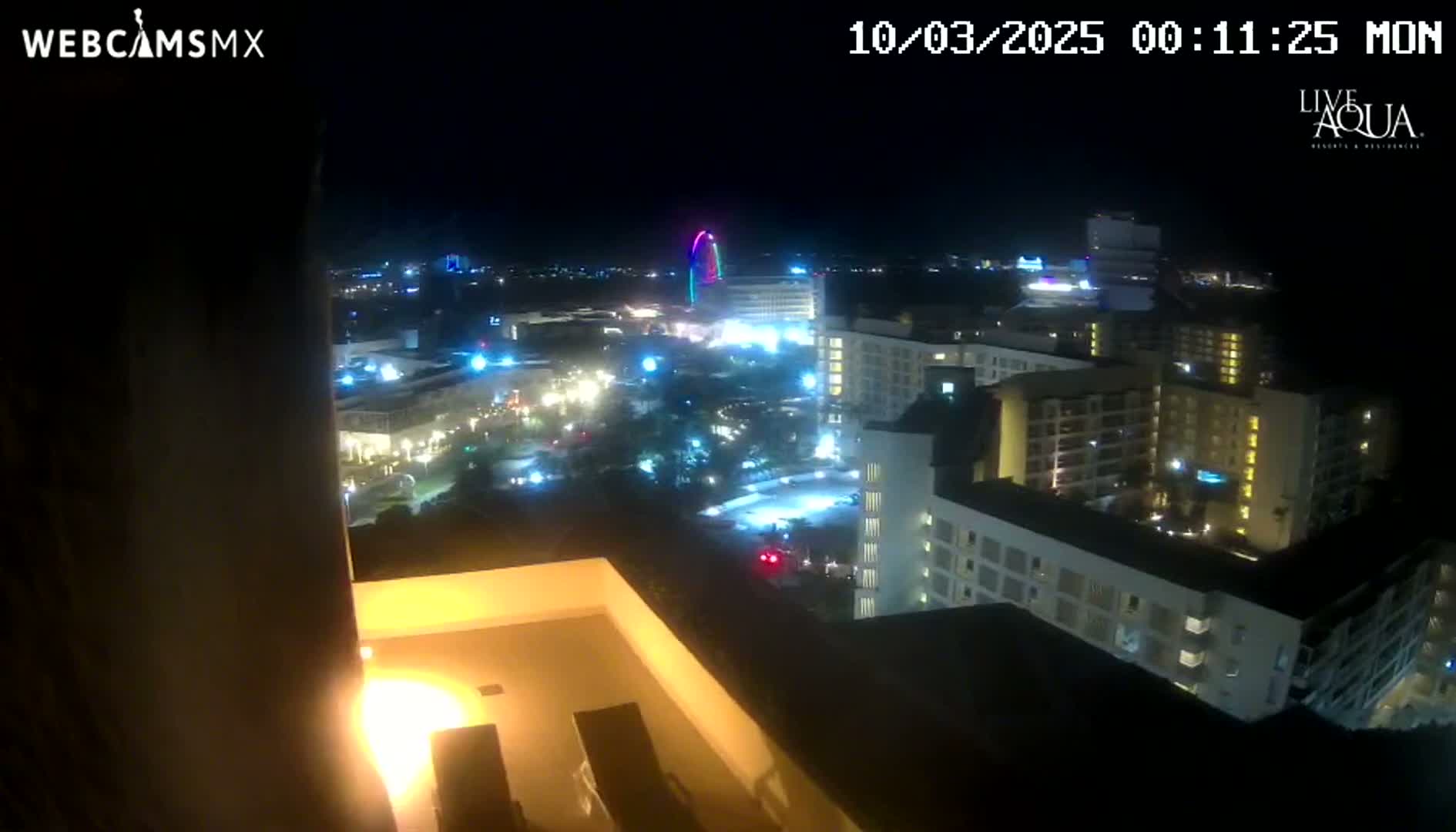 A nighttime, high-angle view shows a brightly lit resort area with multiple hotels and a Ferris wheel, under clear skies.