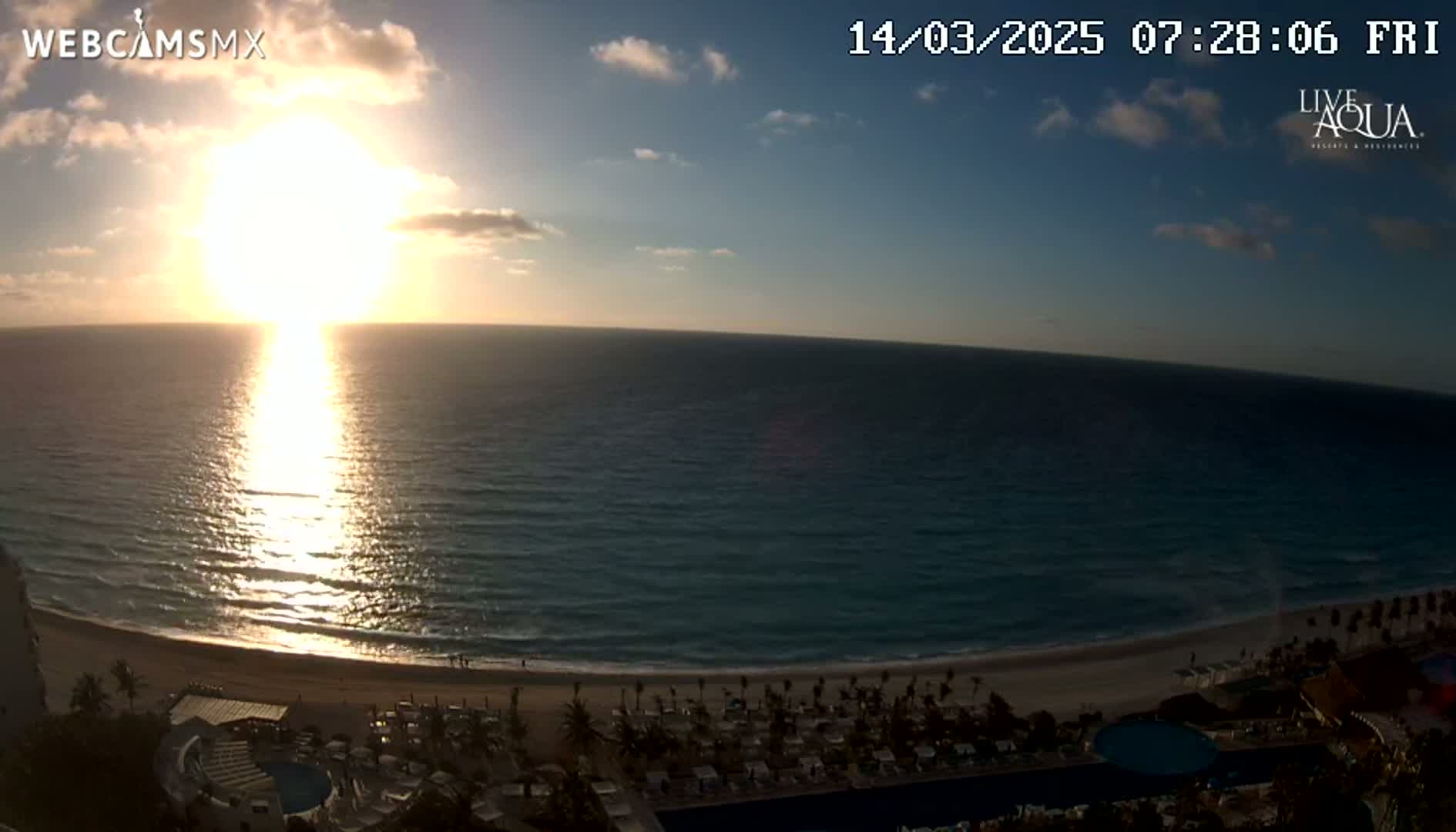 A bright sunrise over a calm ocean, shining on a beach with resort amenities.