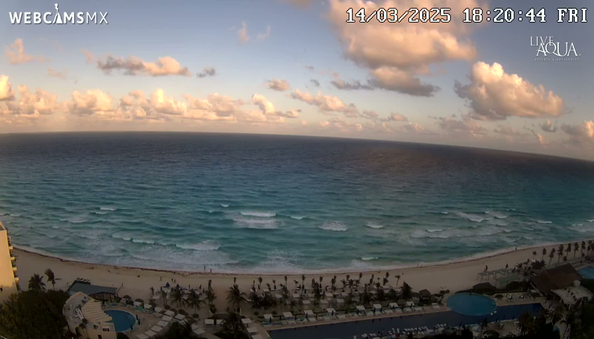 A beach with turquoise water and small waves under a partly cloudy sunset sky.