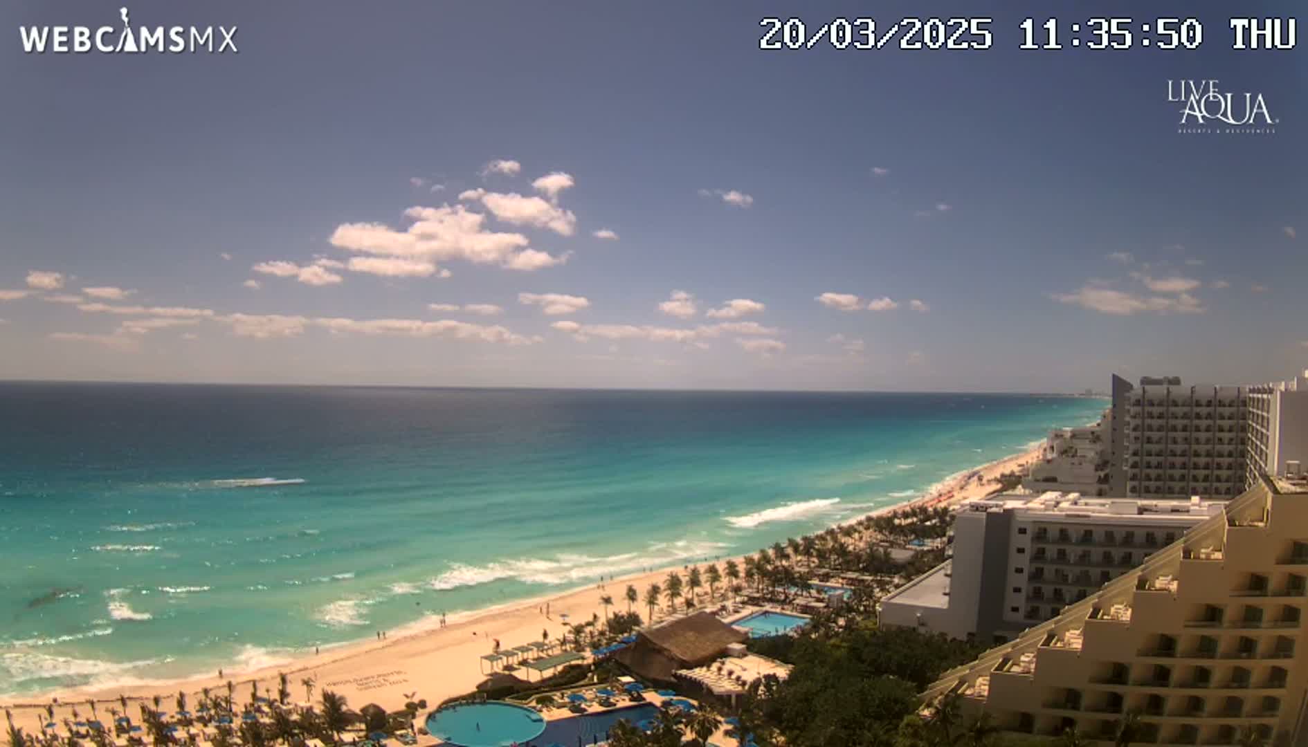 A mostly sunny day reveals a long stretch of turquoise ocean lapping a sandy beach lined with resort hotels.