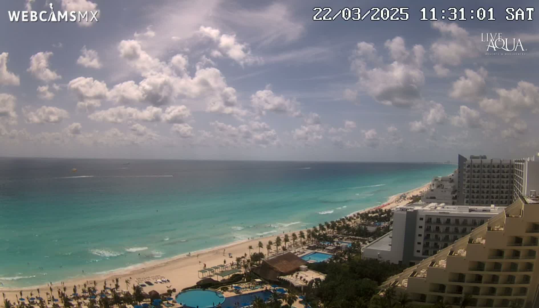 A partly cloudy day shows a long stretch of turquoise ocean meeting a sandy beach lined with hotels and resorts.