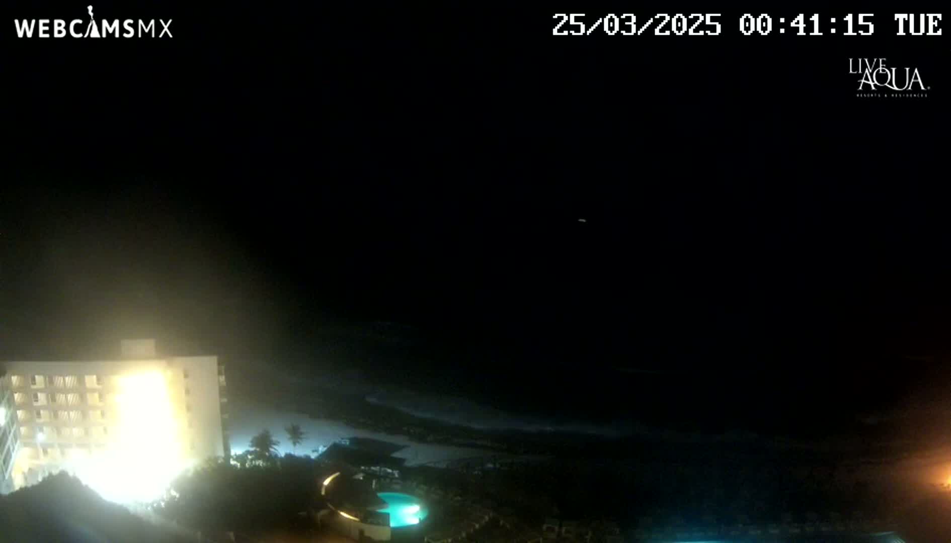 A brightly lit building overlooks a dark, hazy beach at night.