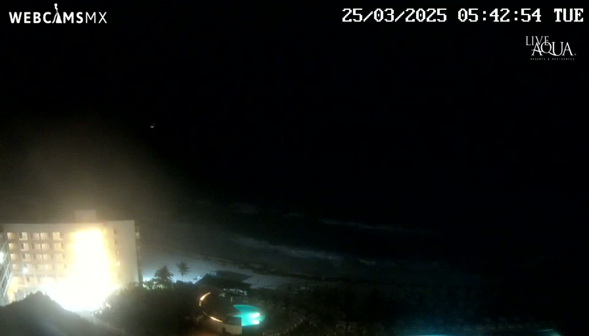A brightly lit building overlooks a dark, wavy ocean at night.
