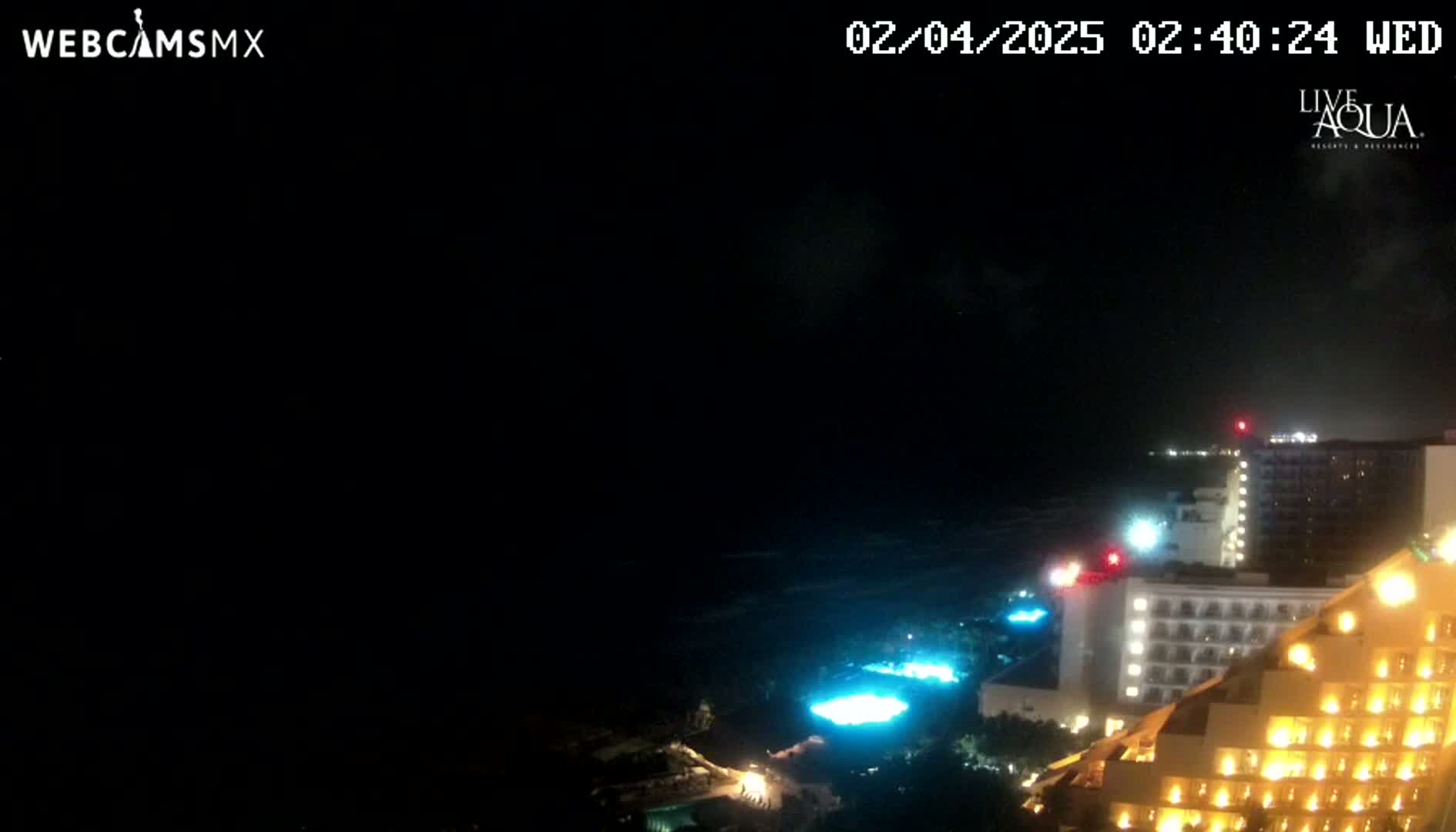 A nighttime view of illuminated buildings along a dark coastline under a cloudy sky.