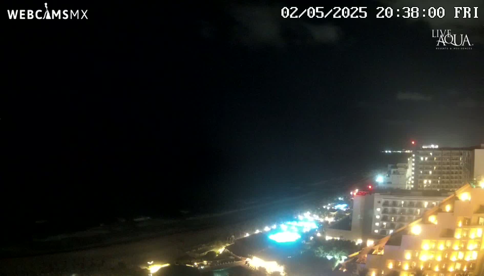 A nighttime view of a beach and illuminated hotels under a mostly clear sky.