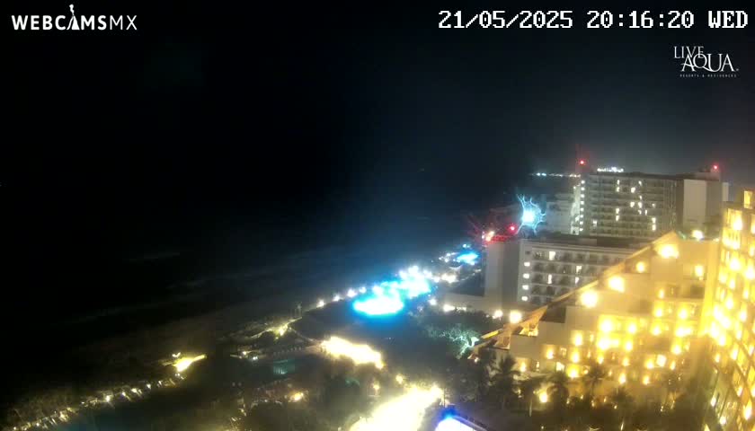 A nighttime coastal scene shows brightly lit hotels and resorts along a dark ocean under a clear sky.