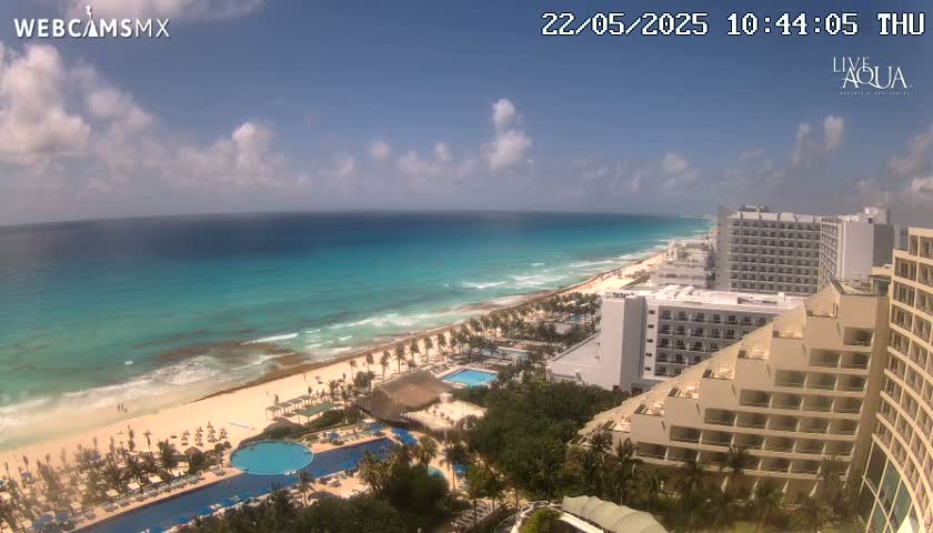 A partly sunny day overlooking a beach with turquoise water, multiple resort hotels, and swimming pools.