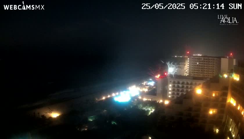 A nighttime view of a beach and brightly lit hotels, with a stormy sky and lightning visible over the ocean.