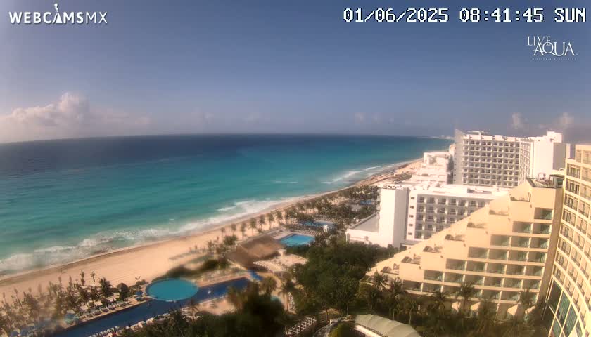A sunny day reveals a beach with turquoise water, hotels, and lush vegetation, overlooking a coastline.