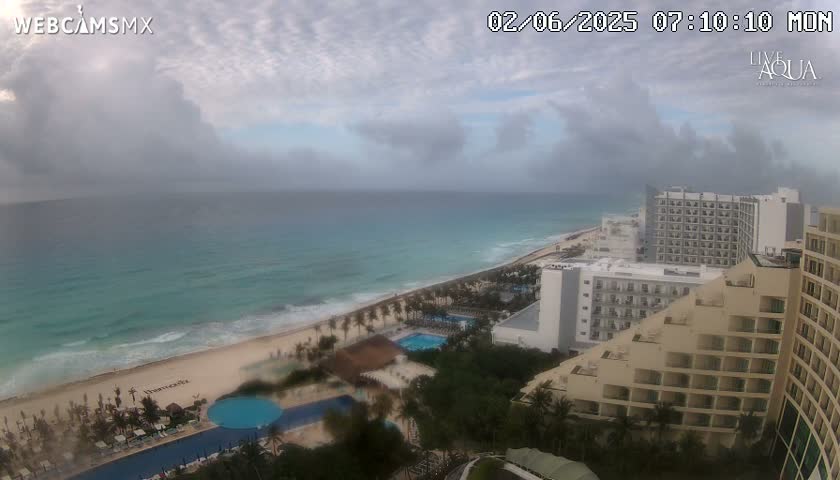 A mostly cloudy day overlooks a tropical beach with turquoise water and several resort hotels.
