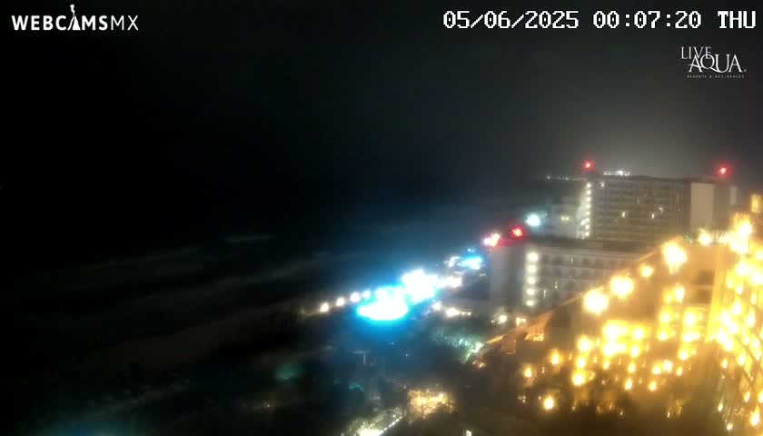 A nighttime, hazy view of brightly lit hotels near a dark ocean.